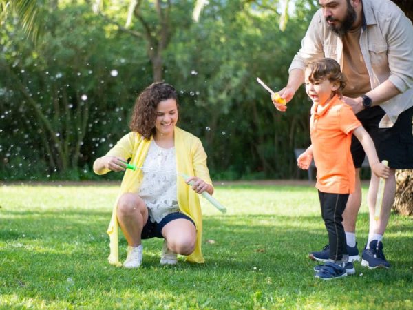 A family enjoys a playful day with bubbles in a sunny park setting.